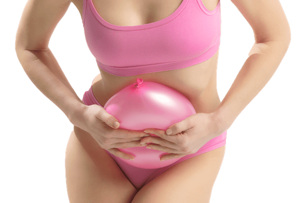 Woman in pink swimsuit holds balloon to belly in indication of discomfort.